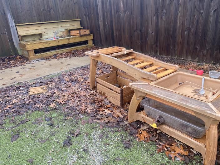 Wooden outdoor pet enclosures and benches in a fenced backyard covered with leaves.