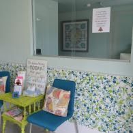 Small waiting area with blue chairs, floral wallpaper, and a windowed reception counter.
