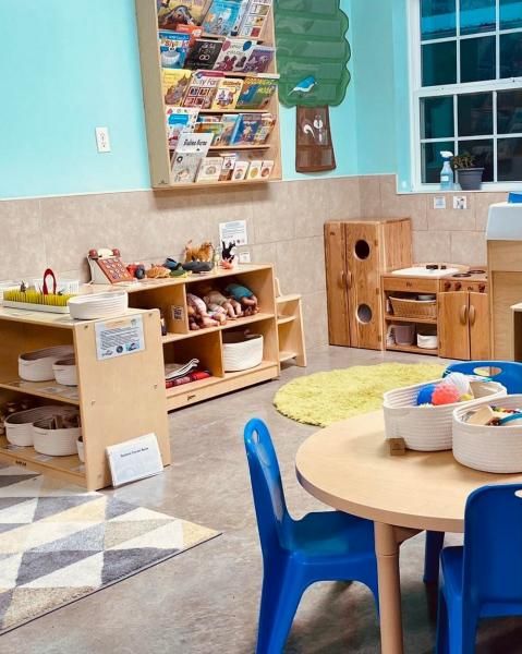 Colorful preschool classroom with tables, shelves, toys, and a window.