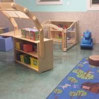 Children’s playroom with toy shelves, blue ride-on toy, and patterned rug on a teal floor.
