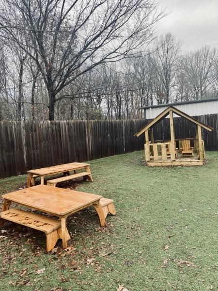 Backyard with wooden picnic tables and a small playhouse, surrounded by a fence and leafless trees.
