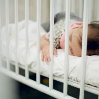 Sleeping baby in a crib with white bedding and gray striped clothing