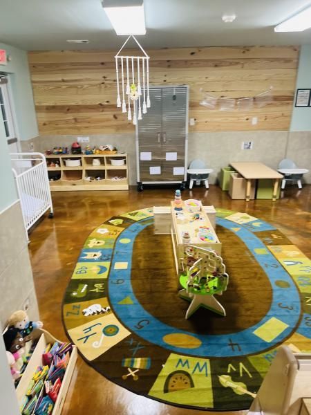 Circular classroom rug in a daycare room with tables, shelves, and toys, centered around a small plant display.