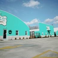 Turquoise warehouse buildings with white trim under a blue sky, viewed across a paved lot