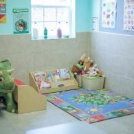 Children’s play corner with toys, books, and a colorful floor mat against pale green tiled walls