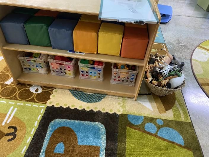 Children’s classroom shelf with colorful storage bins, baskets, and a patterned rug in the foreground