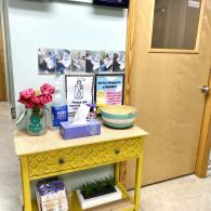 Decorated entry table with flowers, framed signs, bowls, and a wooden door in a hallway