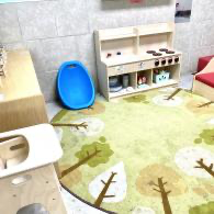 Children’s play area with a blue toy chair, wooden kitchen set, and green tree-pattern rug