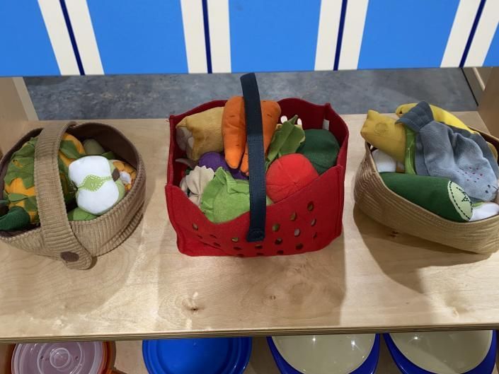 Three small baskets of felt vegetables on a table, including a red basket in the center.