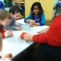 Children gathered around a table with an adult, engaged in a classroom activity with colorful objects
