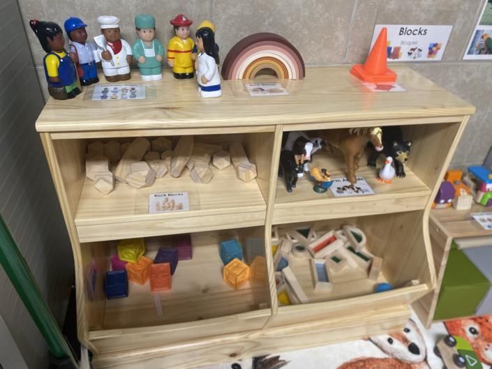 Wooden toy shelf with small figurines, blocks, and colorful toys in a classroom play area