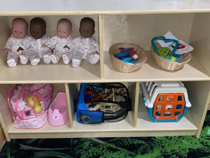 Shelf with baby dolls and baskets of toys in a playroom.