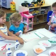 Children doing a table craft with glue and colored paper in a classroom