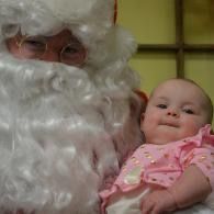 Santa holding a baby in a pink outfit, both close to the camera.