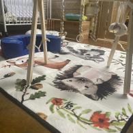 A cat-printed rug under a white play gym with hanging toys in a living room.
