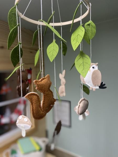 Animal felt mobile hanging from a white ring, with green leaves and small woodland creatures in soft colors
