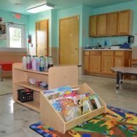 Childcare room with toy shelf, colorful play mat, cabinets, and a door in the background