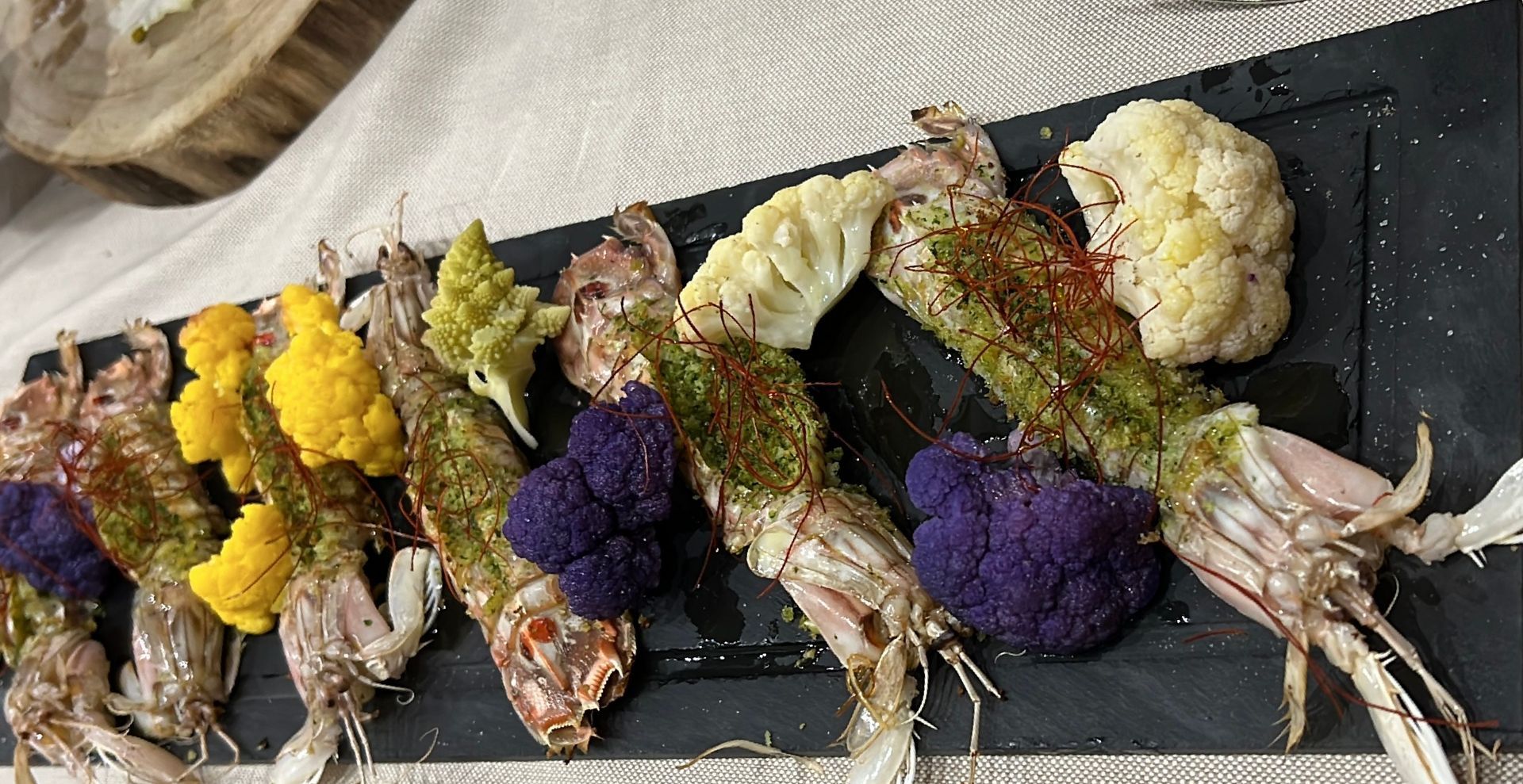 Un piatto nero con sopra gamberi e cavolfiore su un tavolo.