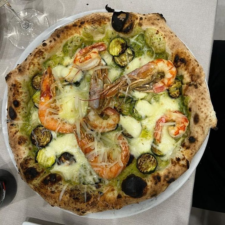 Una pizza con gamberi e zucchine su un piatto bianco