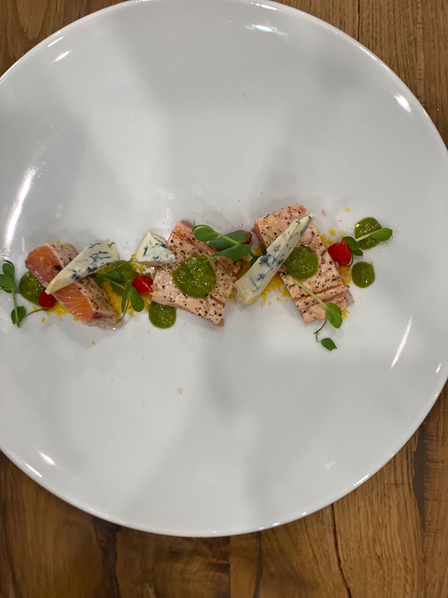 Un piatto bianco con sopra carne e verdure su un tavolo di legno.