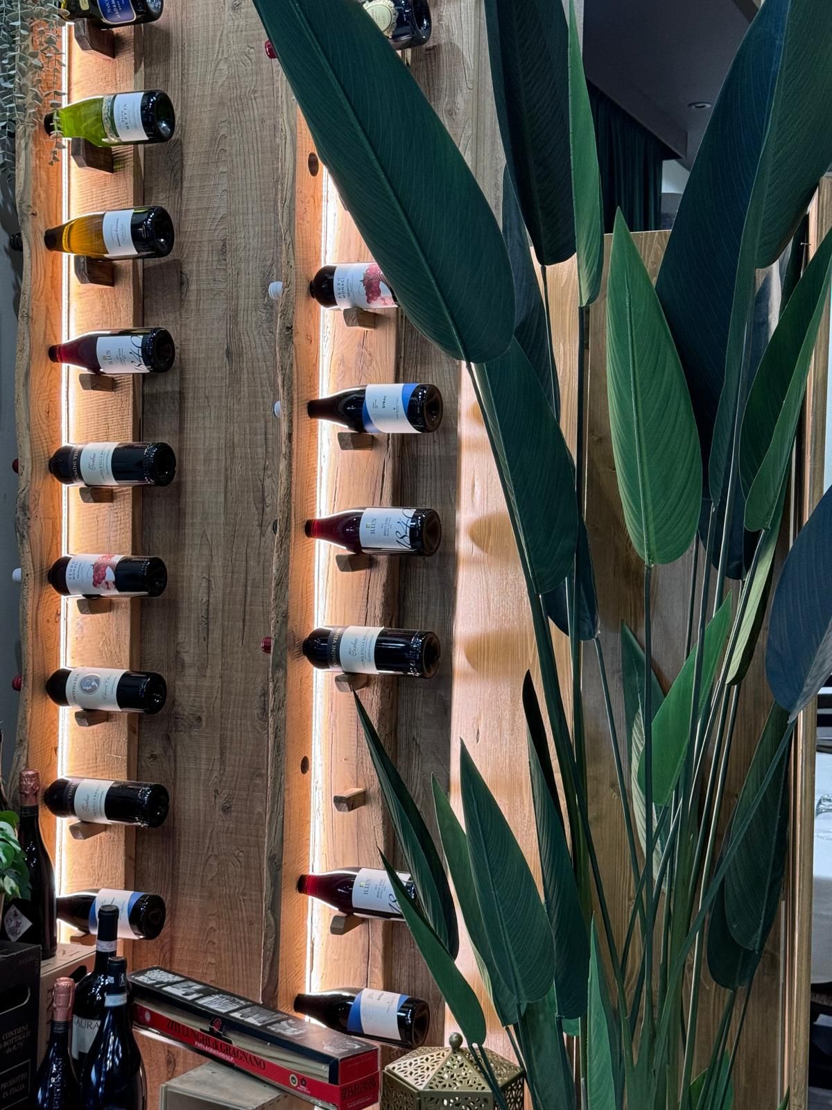 Una fila di bottiglie di vino appese a una parete di legno accanto a una pianta.