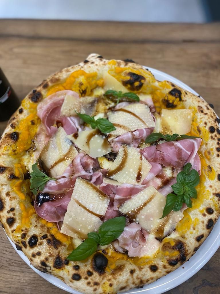 Una pizza è appoggiata su un piatto bianco su un tavolo di legno.