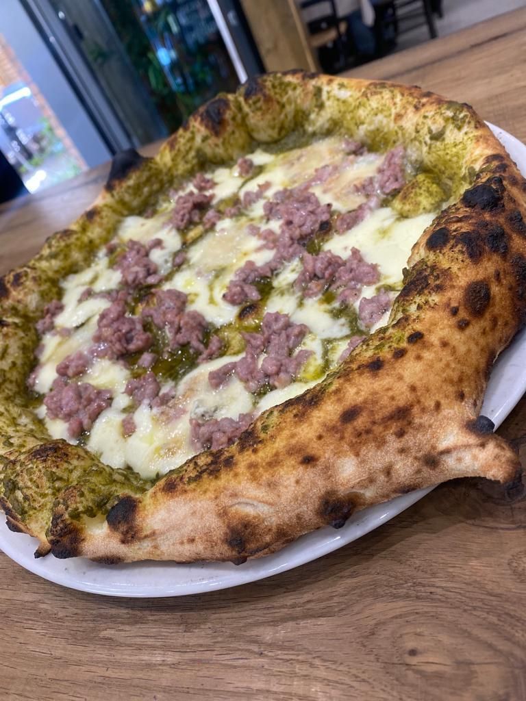 Una pizza è appoggiata su un piatto bianco su un tavolo di legno.
