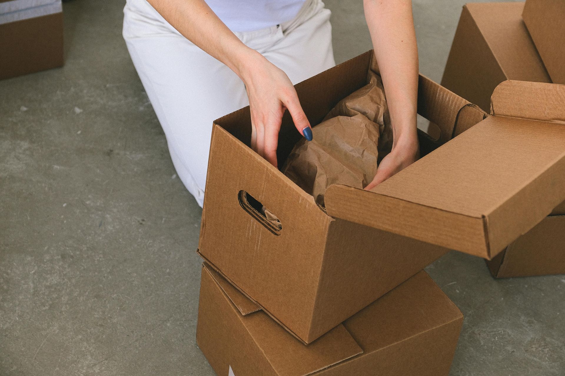 A woman is kneeling down and opening a cardboard box.