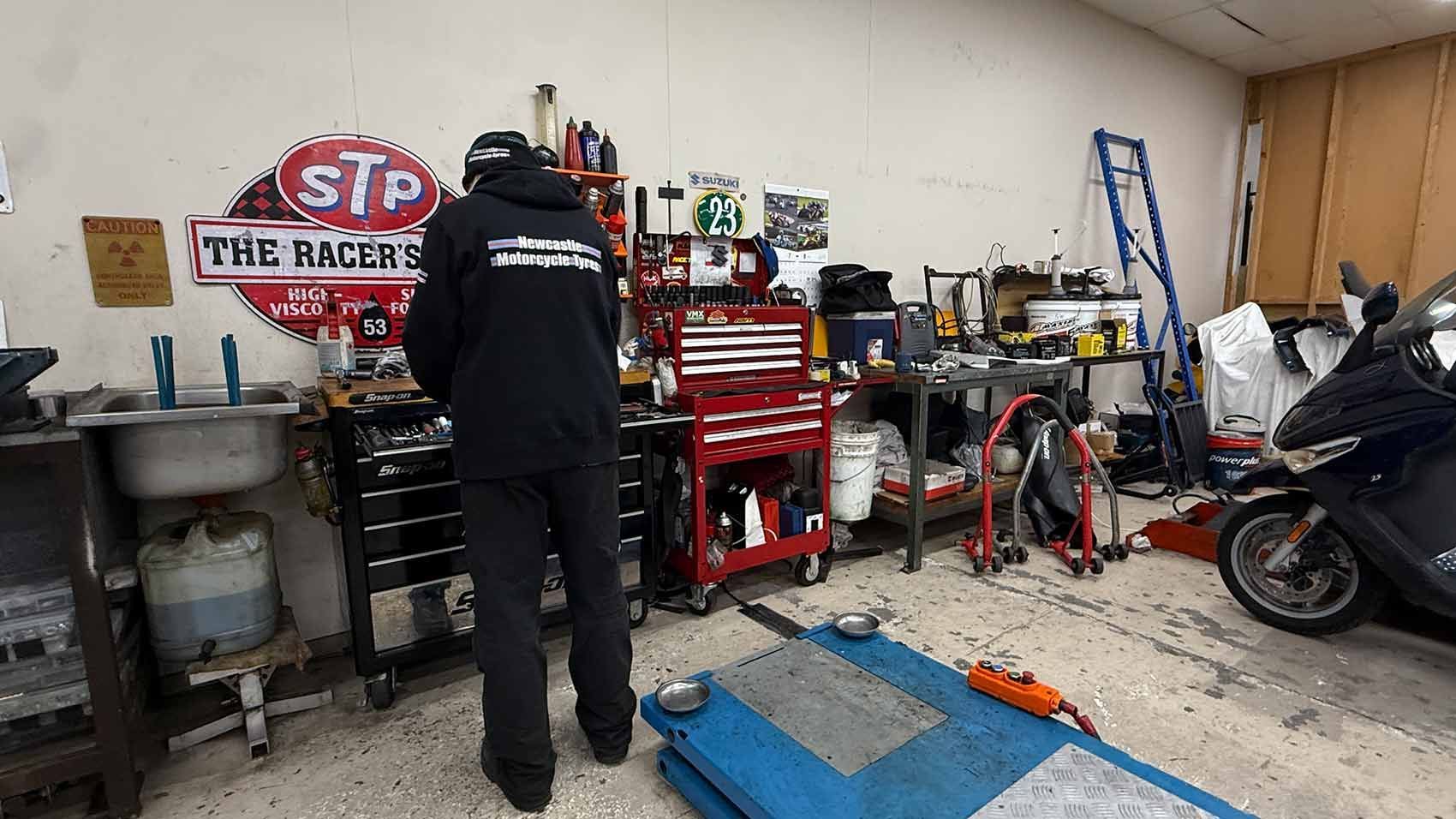A Person in a Black Hoodie Works in a Cluttered Garage Workshop — Newcastle Motorcycle Tyres in Broadmeadow, NSW