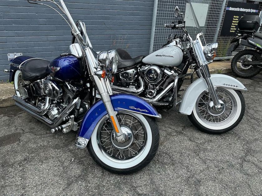 Two Harley Davidson motorcycles, one blue, one white, parked outdoors.