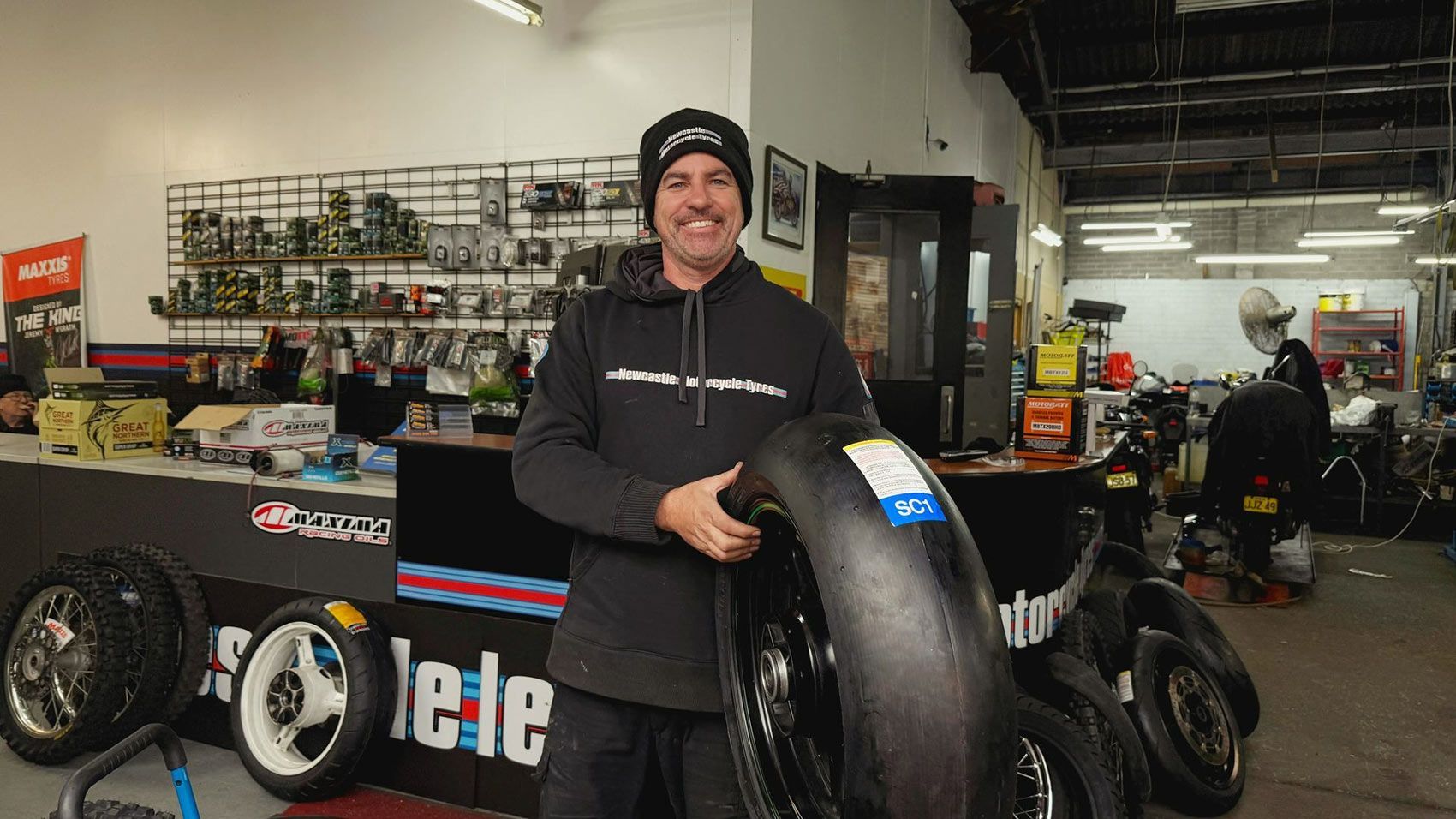 Man in a Shop Holding a Large Motorcycle Tire — Newcastle Motorcycle Tyres in Broadmeadow, NSW