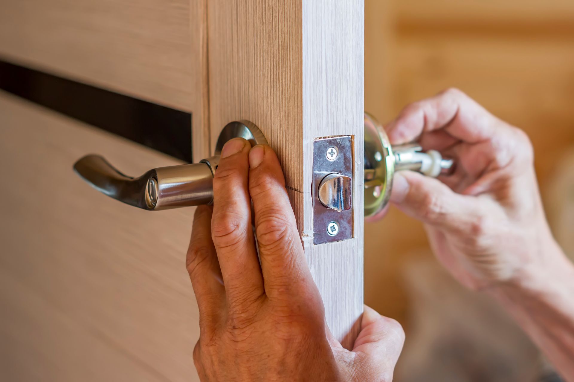 Hands installing a silver door handle on a wooden door close-up