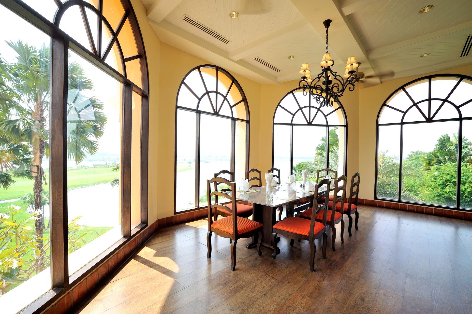 Elegant dining room with arched windows, chandelier, and a table set by a bright garden view