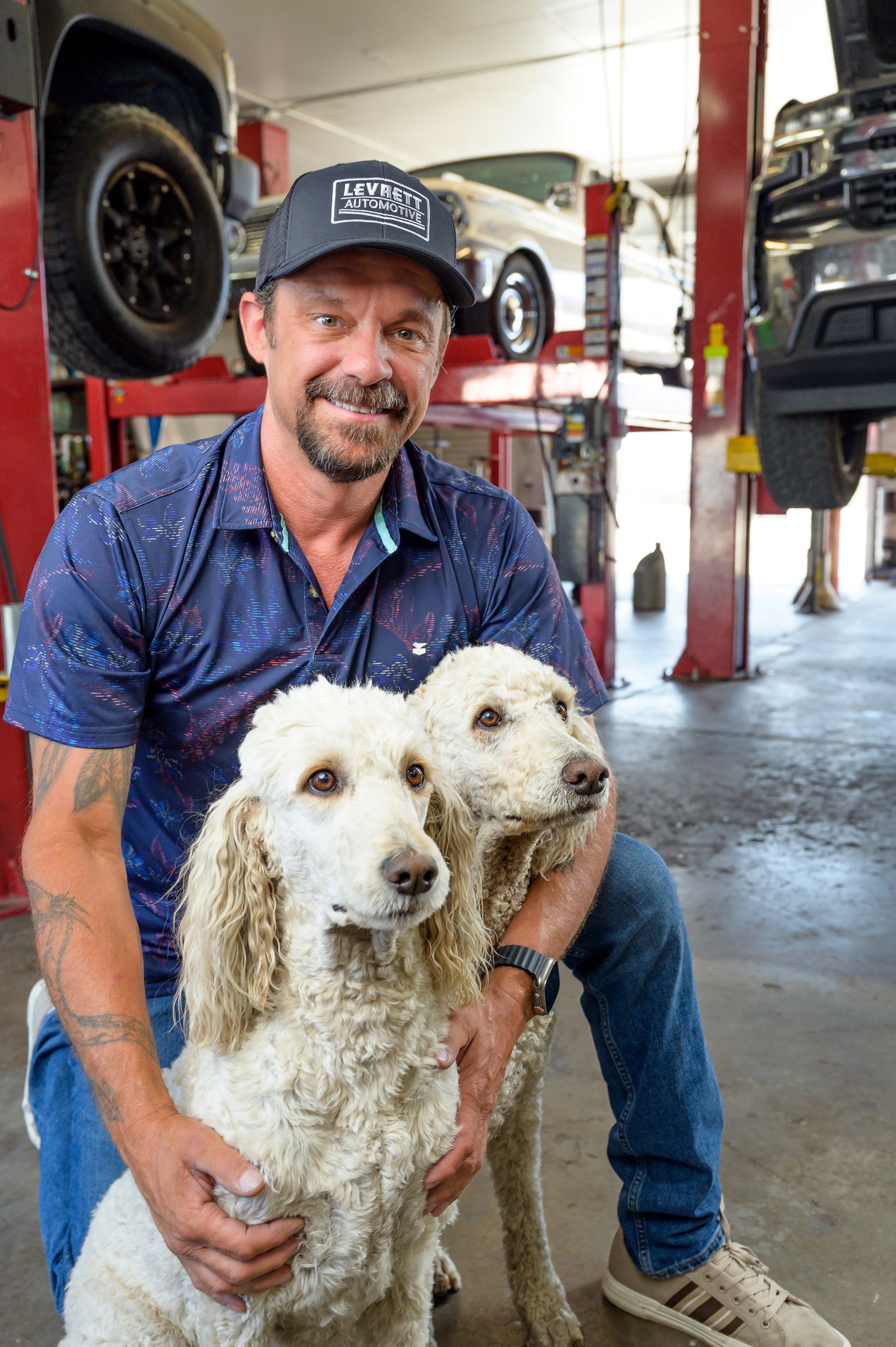 A man is sitting next to two dogs in a garage.