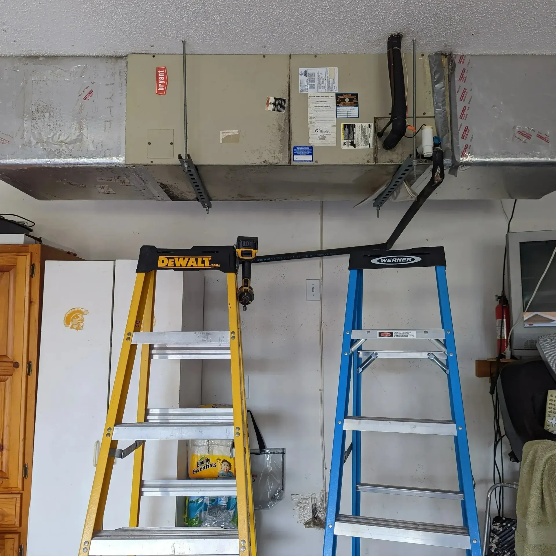 Hvac-Contractor-Bradenton-Two ladders support a black pipe near an air handler in a garage.