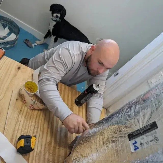 Hvac-Contractor-Bradenton-Man installing insulation, black and white dog watches from above.