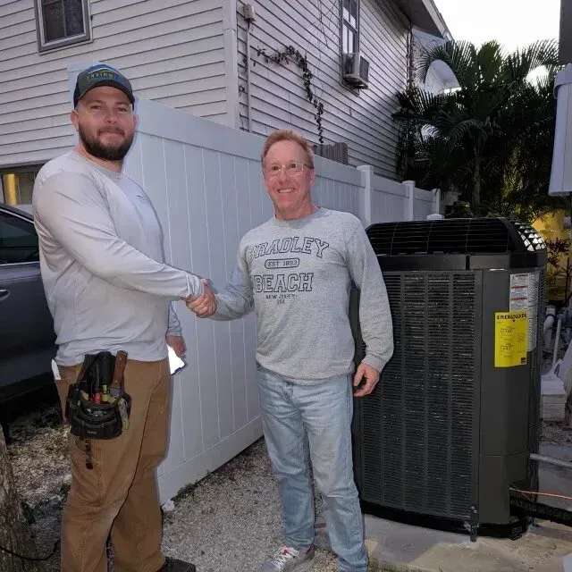Hvac-Contractor-Bradenton-Two men shake hands in front of a new AC unit, white fence, and house. One man is wearing work clothes.