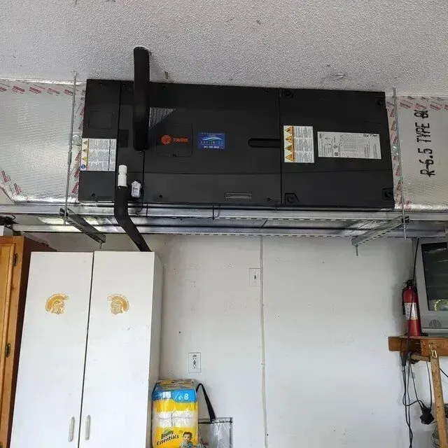 Hvac-Contractor-Bradenton-HVAC unit mounted in a garage ceiling, above a white cabinet and an old TV.