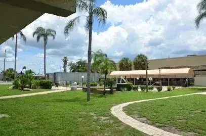 Hvac-Contractor-Bradenton-Green lawn with a winding walkway, palm trees, and low buildings under a cloudy sky.