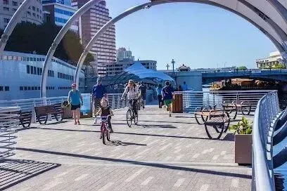 Hvac-Contractor-Bradenton-People biking and walking on a waterfront boardwalk under archways, sunny day.