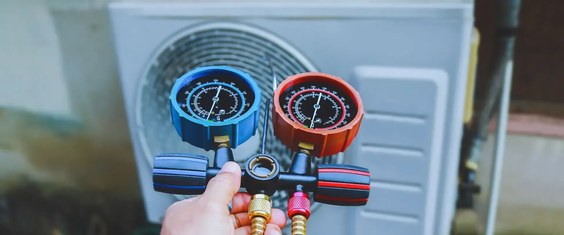 A person is holding a gauge in front of an air conditioner.