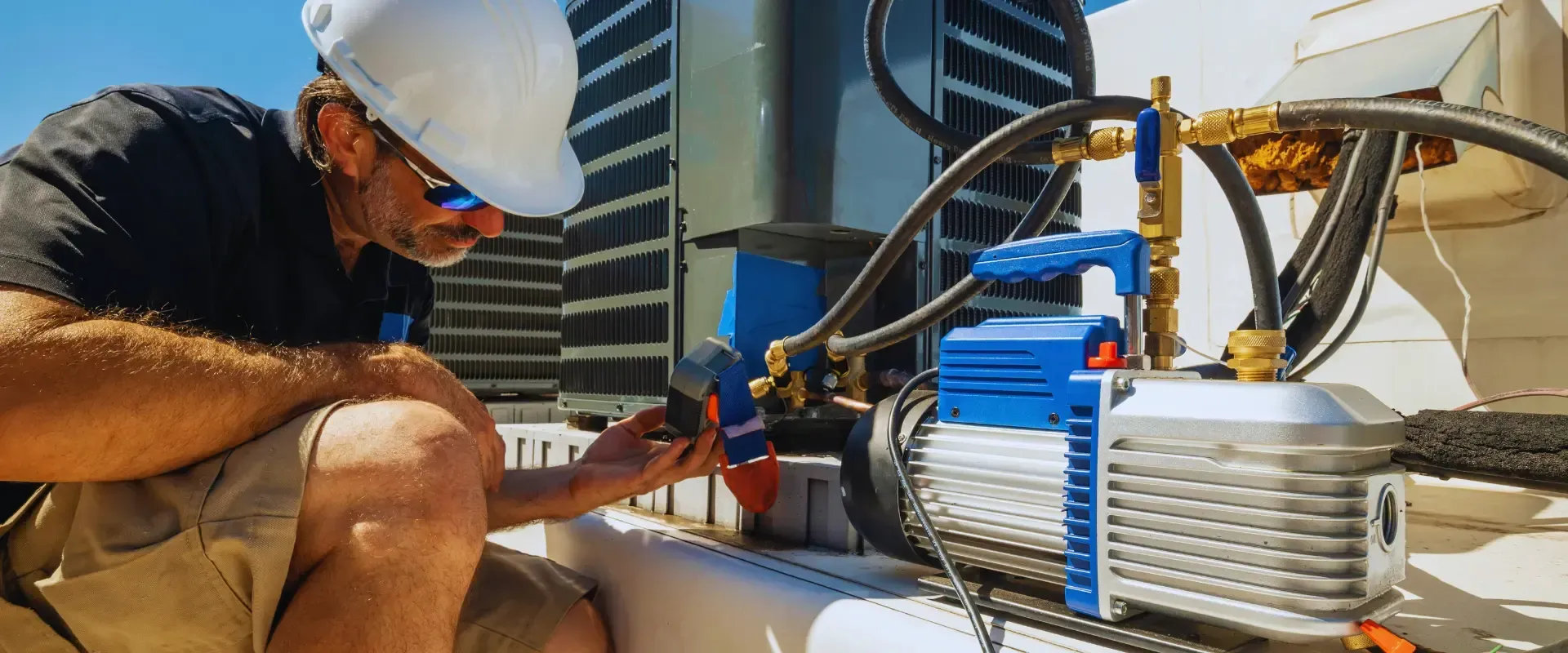 A man wearing a hard hat and sunglasses is working on an air conditioner.