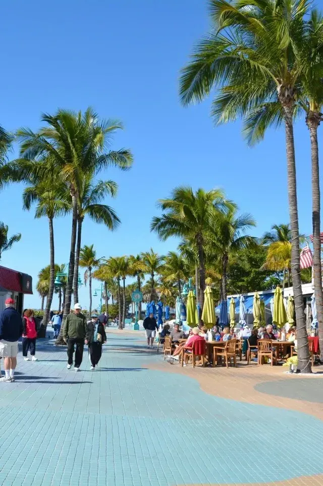 hvac-contractor-People stroll along a sunny waterfront promenade lined with palm trees and outdoor restaurants.