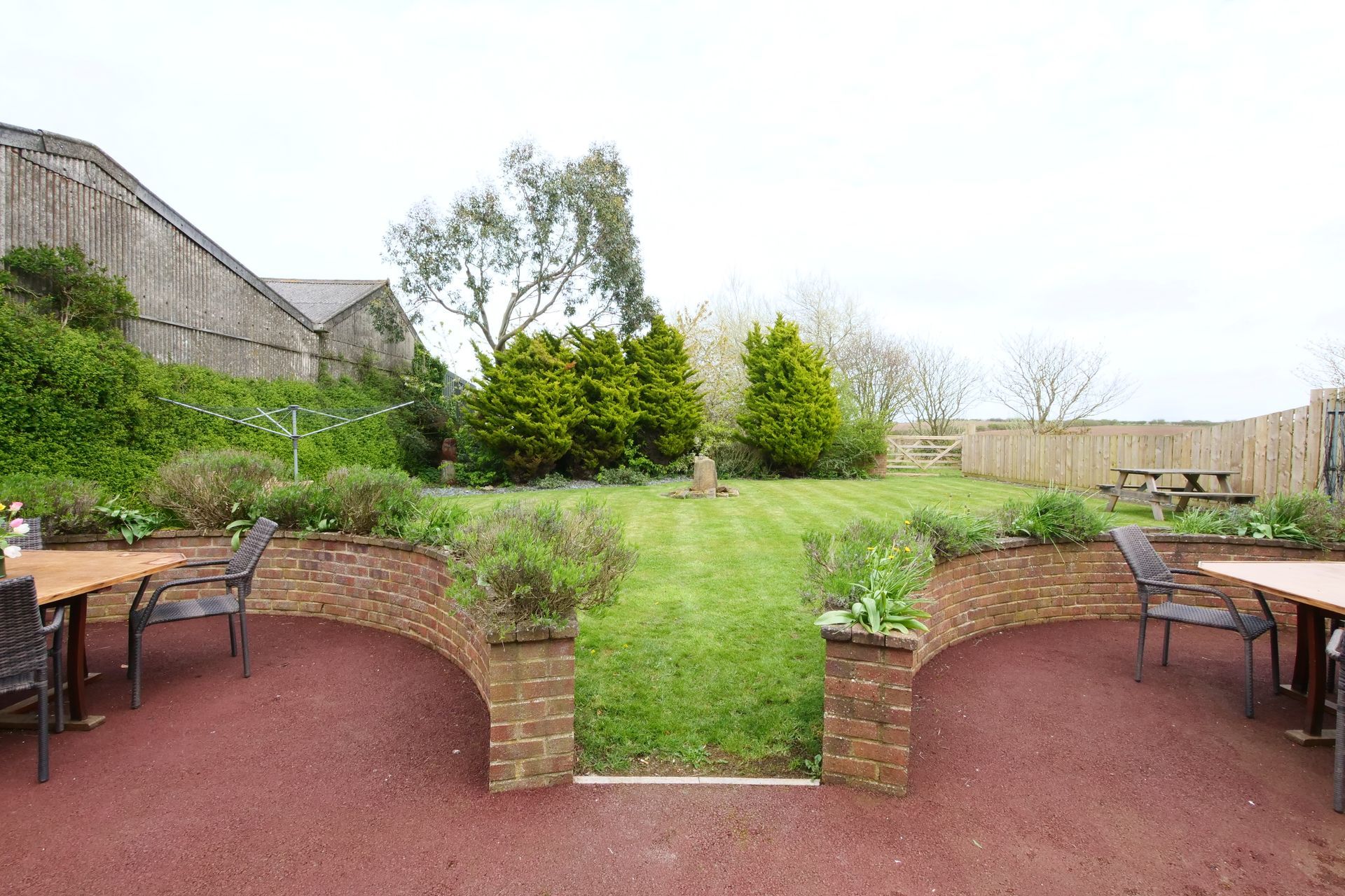A patio with tables and chairs in front of a lush green garden.