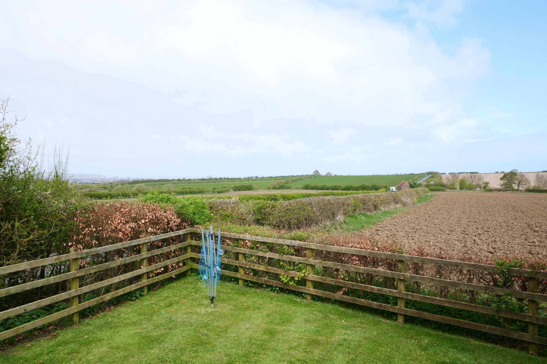 A wooden fence surrounds a lush green lawn with a view of a field.