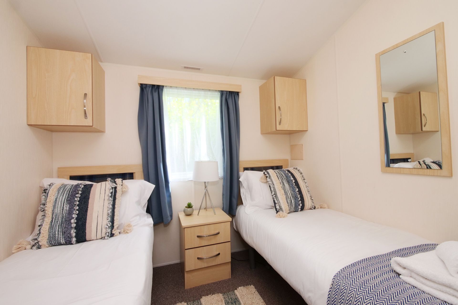 A bedroom with two beds , a nightstand and a mirror.