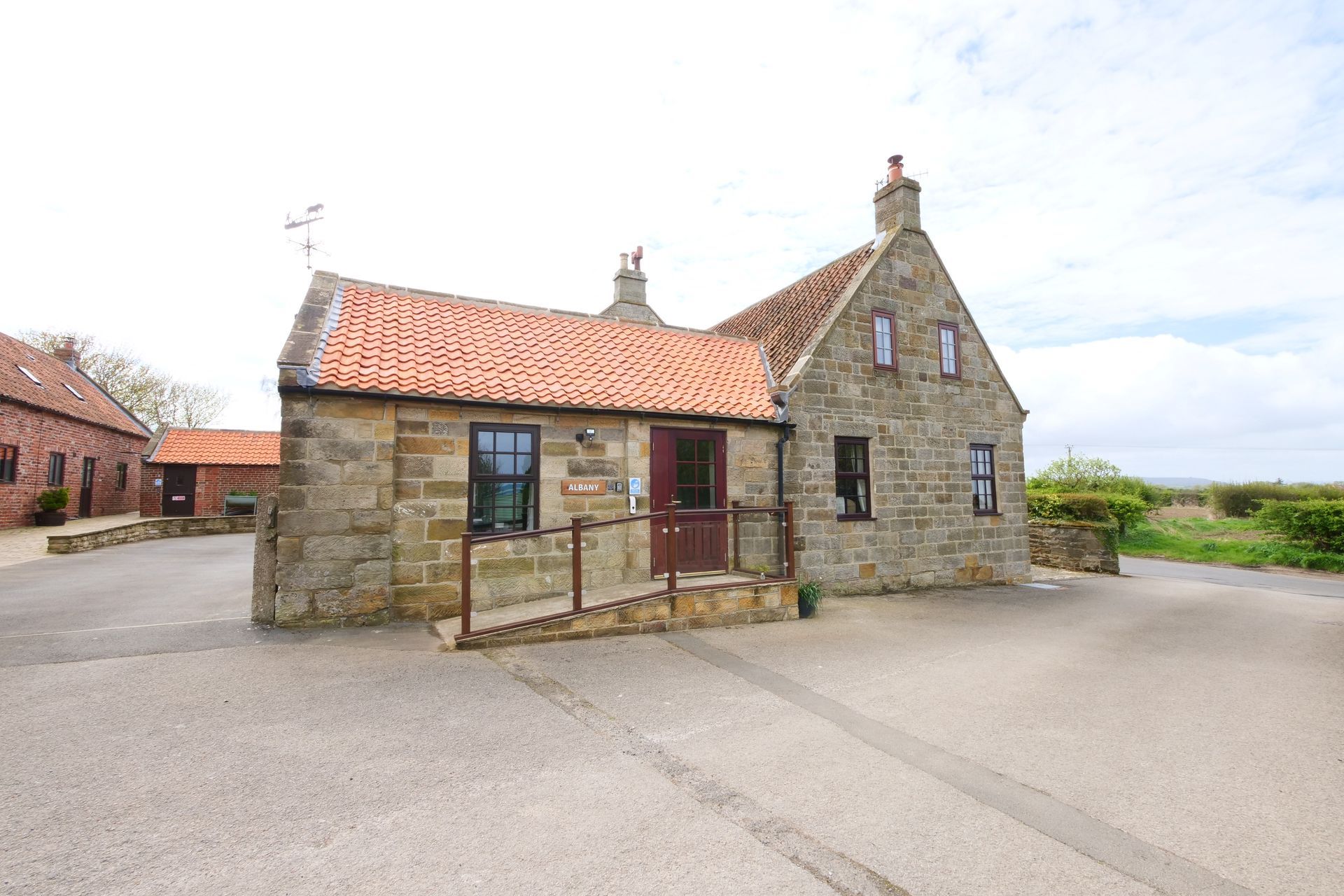 A small stone house with a red roof and a ramp in front of it.