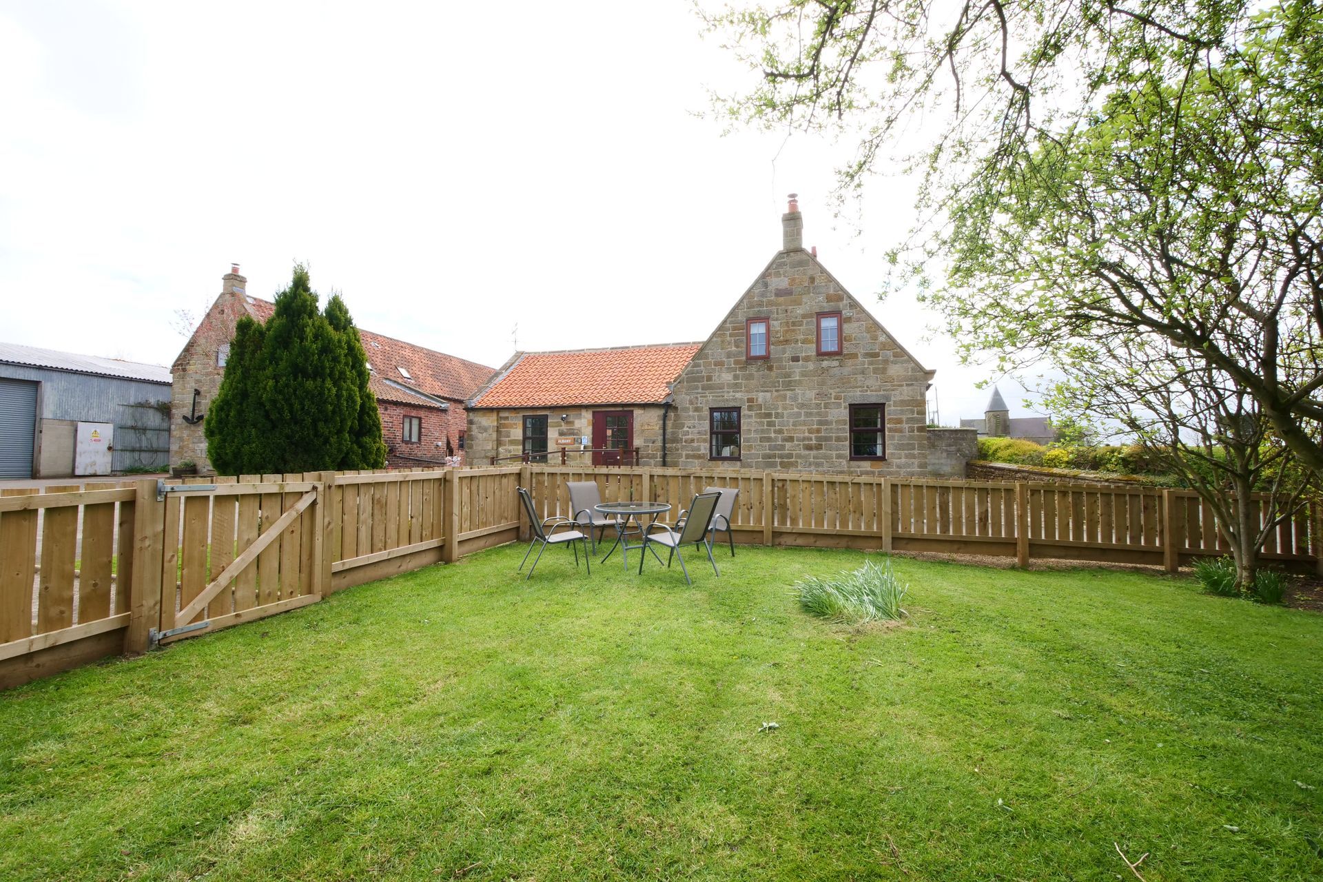 A large backyard with a wooden fence and a stone house in the background.