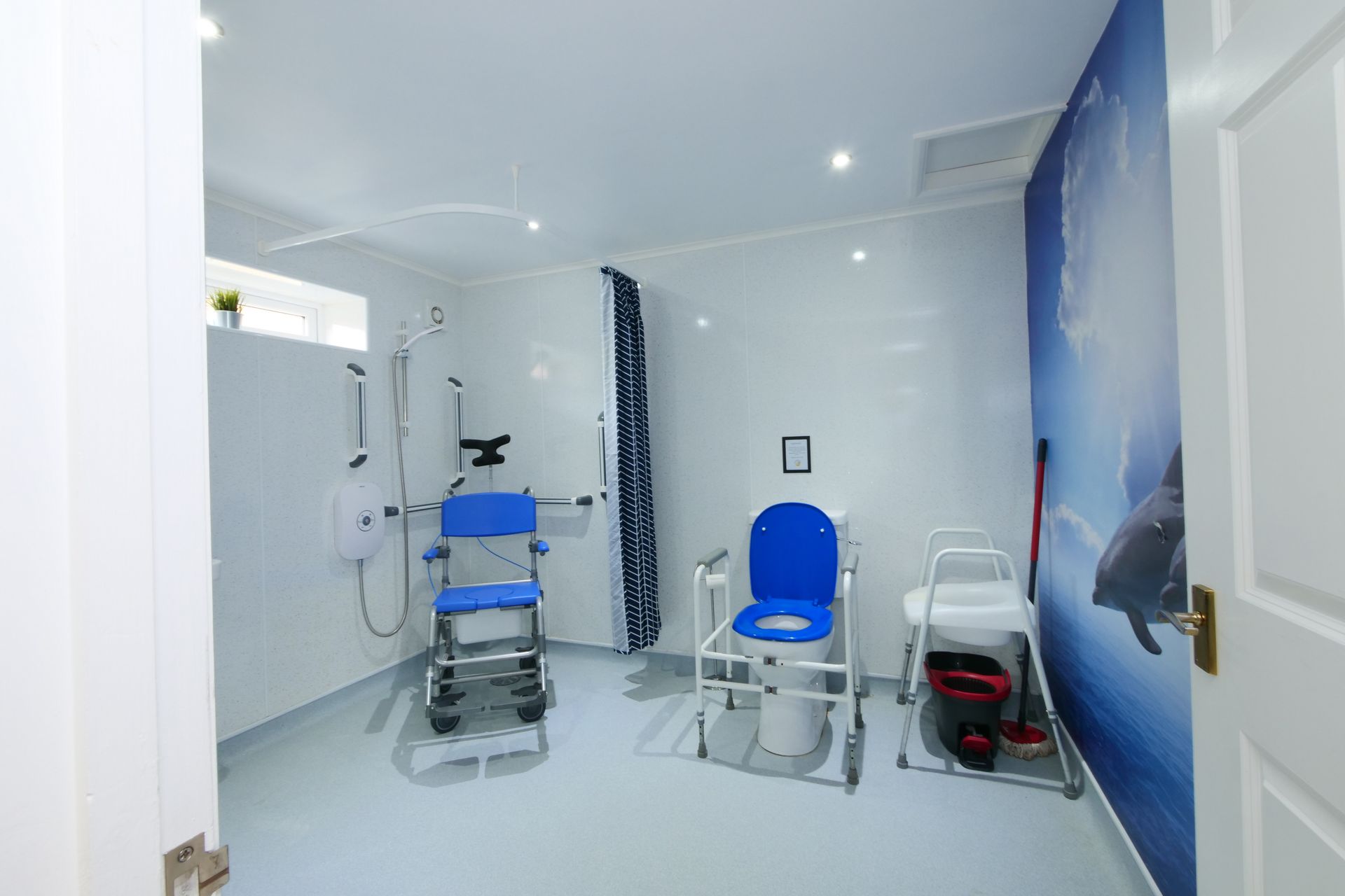 A bathroom with a blue chair , toilet and shower.