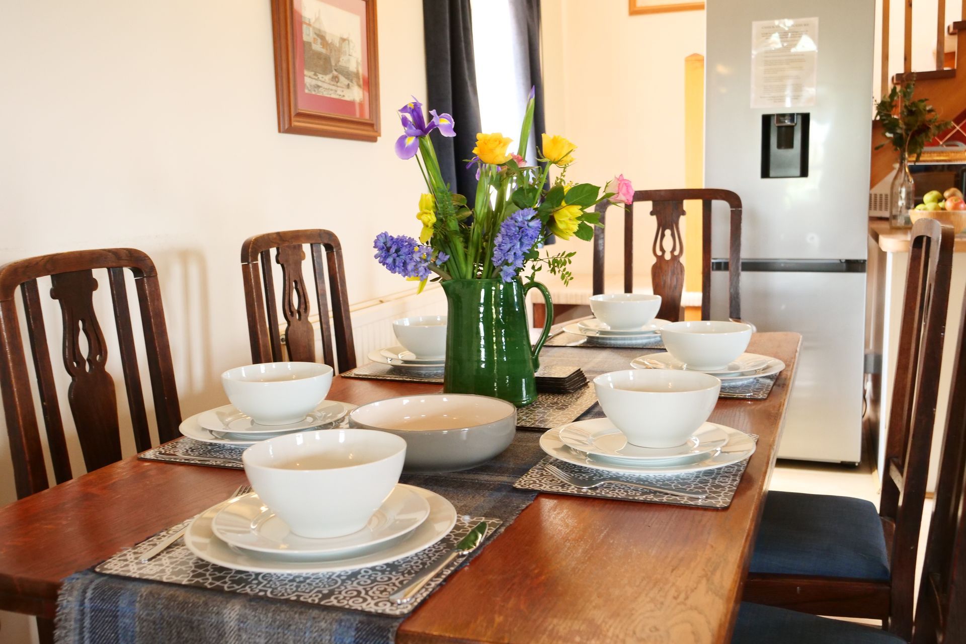 A dining room table with bowls and plates and a vase of flowers on it.